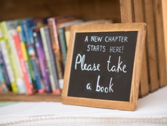 Small chalkboard with "Please Take a Book" written, sitting in front of a small bookshelf