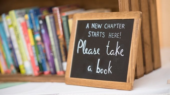 Small chalkboard with "Please Take a Book" written, sitting in front of a small bookshelf