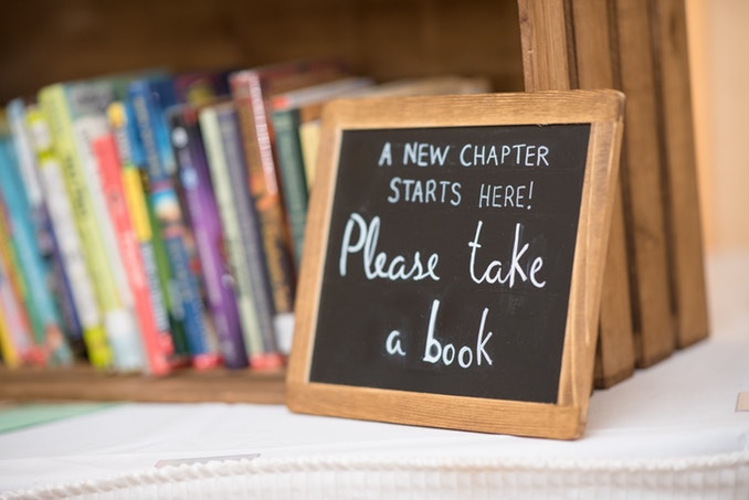 Small chalkboard with "Please Take a Book" written, sitting in front of a small bookshelf